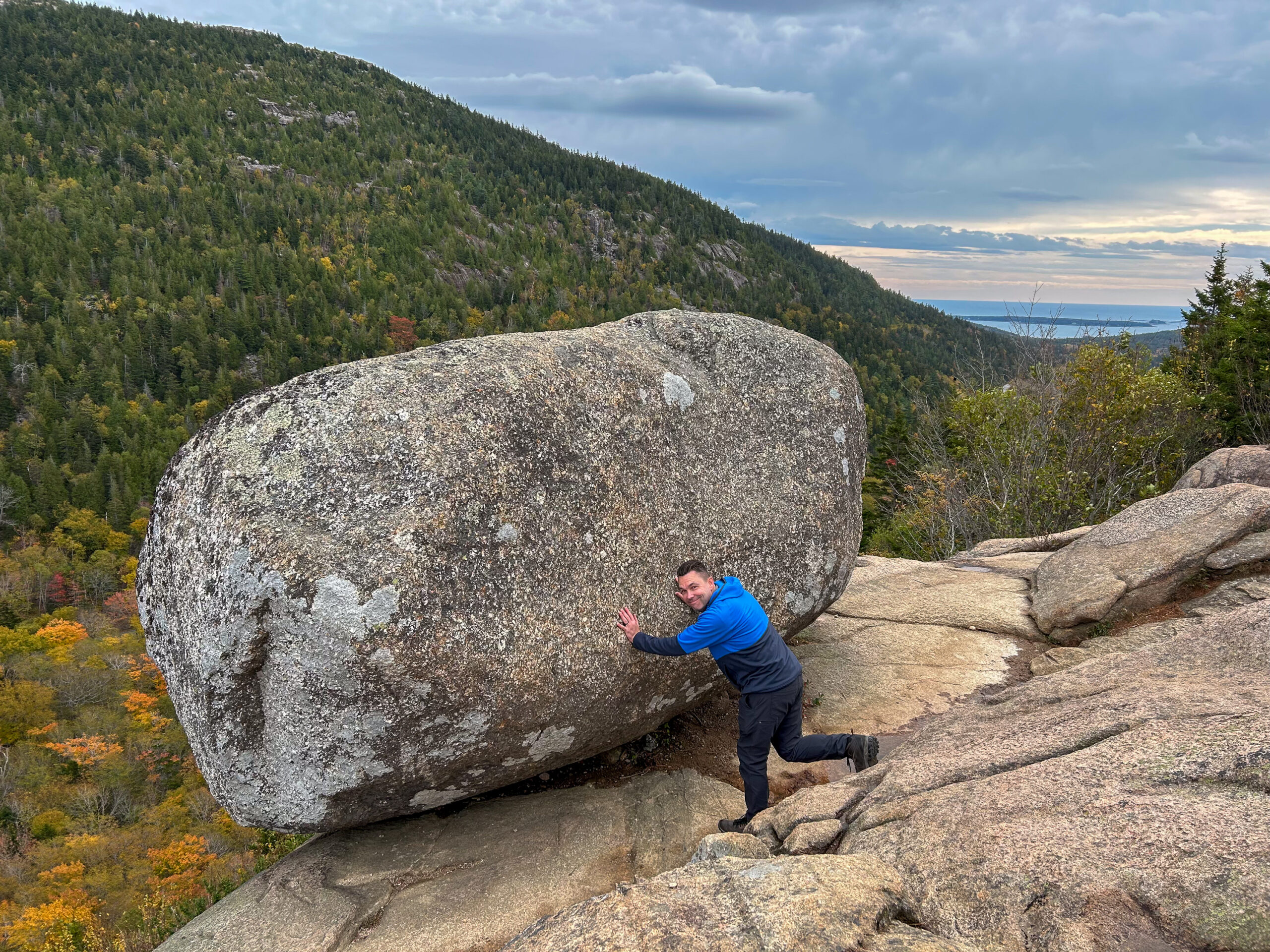 Person playfully pushing Bubble Rock on South Bubble in Acadia National Park