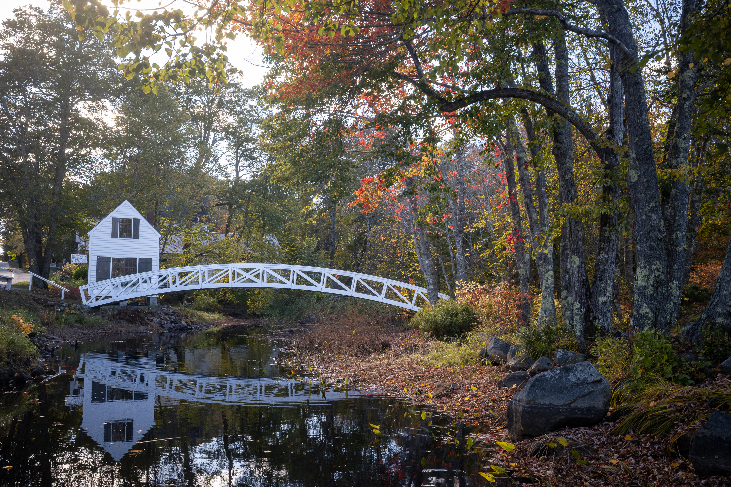 Somesville Bridge in Mount Desert Maine reflected in a calm stream with fall foliage in Acadia National Park