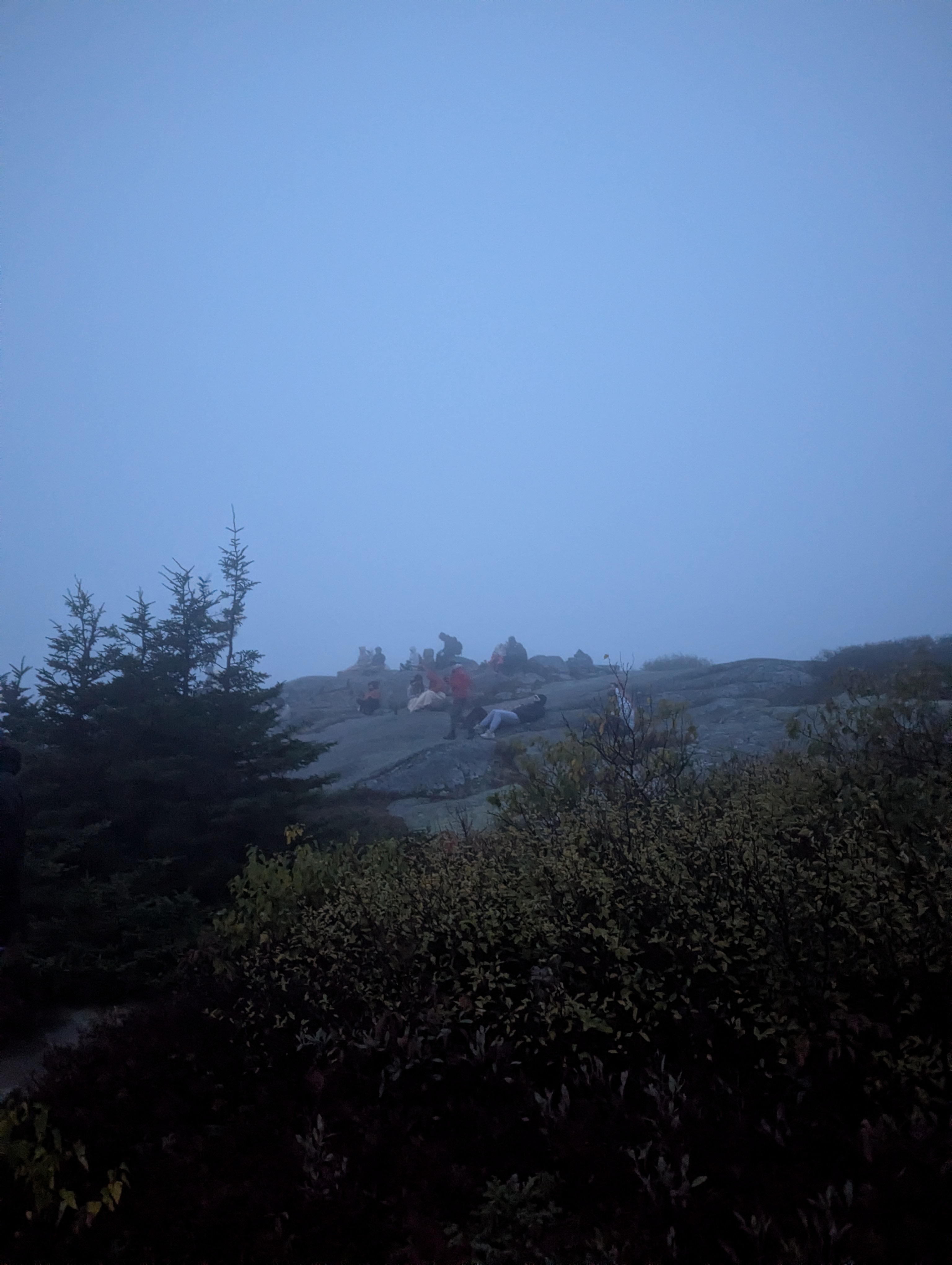 Visitors gathered at Cadillac Mountain summit during low visibility sunrise conditions in Acadia
